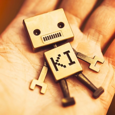 Symbol: Eine Roboterspielfigur mit Aufschrift KI liegt auf einer menschlichen Hand.