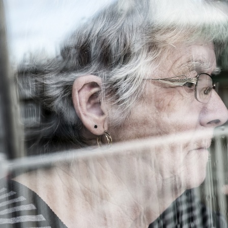 Eine ältere Frau schaut aus einem Fenster.