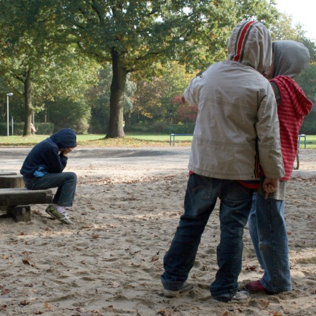 Zwei Kinder zeigen auf einem Spielplatz mit dem Finger auf ein anderes Kind