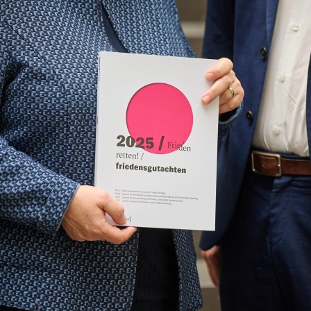 Eine Frau hält das Friedensgutachten &#034;Frieden retten!&#034; 2025 in den Händen.