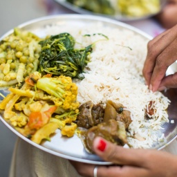 Indischer weiblich essender traditionelle dish mit rice, peas, Fleisch und Gemüse. Symbolfoto