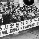 "Herzlich Willkommen in Frankfurt Deutschland" steht auf einem Spruchband, mit dem eine große Gruppe Krankenschwestern aus Südkorea im Jahr 1966 auf dem Rhein-Main-Flughafen begrüßt wird. 