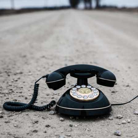 Ein altes Telefon steht einsam auf einer staubigen Straße.