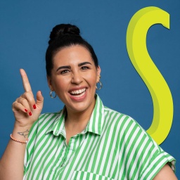 Ariana Baborie lachend mit Finger nach oben zeigend vor blauem Hintergrund „S“