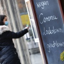 Eine Frau steht vor einem Laden, vor dem eine Tafel steht mit der Aufschrift: "Wegen Corona Lockdown geschlossen."