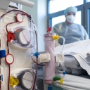Ein Krankenpfleger steht am Bett eines Intensivpatienten hinter einem Dialysegerät.