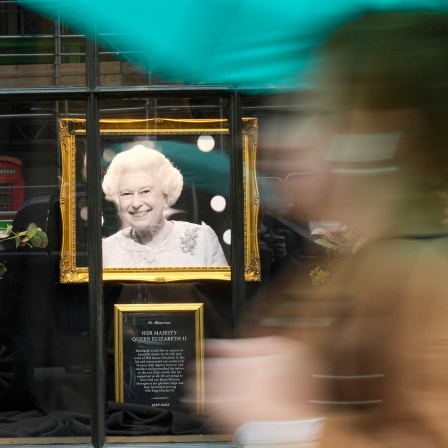 Eine Frau geht an einem Shcaufenster vorei, in dem ein Porträt von Elizabeth II. aufgestellt ist (London, 13.09.2022)