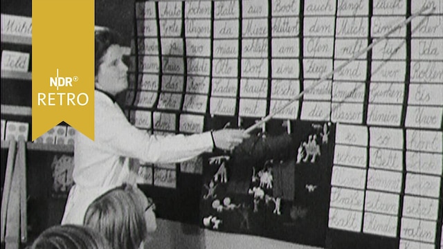 Lehrerin zeigt Kindern an einer mit Klebezetteln bestickten Schultafel Worte (1965)