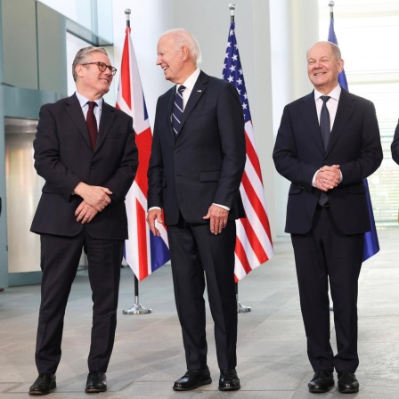 Der britische Premierminister Keir Starmer, US-Präsident Joe Biden, der französische Staatspräsident Emmanuel Macron und Bundeskanzler Olaf Scholz posieren lächelnd für ein Foto. Hinter ihnen die Landesflaggen.