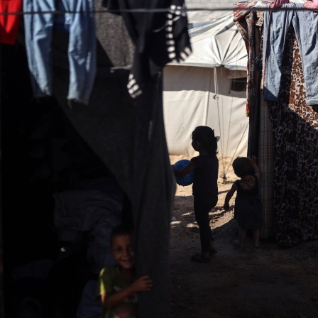 Kinder spielen in einem Flüchtlingscamp im Schatten zwischen Zelten und aufgehängter Wäsche