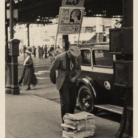 Unter der 6th Avenue steht ein Mann, der eine Werbetafel auf den Rücken geschnallt hat. Er beugt sich leicht nach vorne und liest die oberste Zeitung eines Zeitungsstapels.