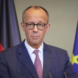 Bundeskanzler Friedrich Merz steht an einem Rednerpult, im Hintergrund sieht man im Anschnitt eine Deutschland- und eine Europa-Flagge.