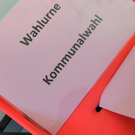 Eine Wählerin steckt ihren Stimmzettel bei einer Kommunalwahl in die Wahlurne.