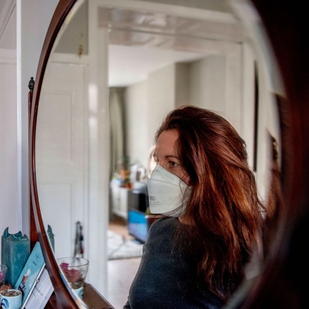 Eine junge Frau mit einer Atemschutzmaske betrachtet sich im Spiegel