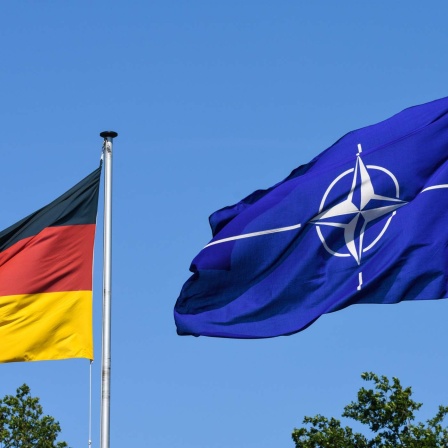 Die wehende Flagge der NATO und im Anschnitt eine Deutschlandflagge an der Zufahrt zum Fliegerhorst.