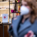 Ein Schild am Eingang eines Schuh-Geschäfts in der City-West weist auf die Pflicht zum Tragen einer FFP2-Maske hin, während im Vordergrund eine Frau mit FFP2-Maske vorbeigeht. Seit 18. Februar entfällt in Berlin die 2G-Regel für den gesamten Einzelhandel.