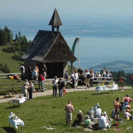 Die Besucher des evangelischen Berggottesdienstes am 15. Juli 2007 auf der Steinlingalm unterhalb des Gipfels der Kampenwand bei Aschau im Chiemgau genießen den Blick auf den Chiemsee. Vor der Kapelle ist ein Biertisch als Altar aufgebaut.