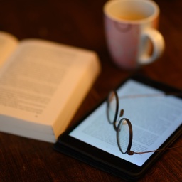 Ein Buch und ein iPad Tablet mit geöffneten eBook liegt auf einem Tisch (Symbolbild)