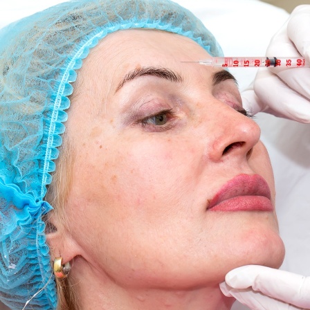 Einer Frau wird eine Substanz mit einer Injektionsspritze in die Stirn injiziert.