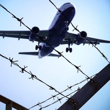 Ein Flugzeug fliegt über einen Stacheldrahtzaun