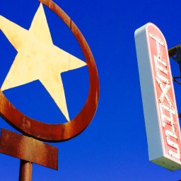 Ein rostiger Texas Lone Star und ein Texas-Schriftzug in Leuchtschrift vor einem intensivblauen Himmel.