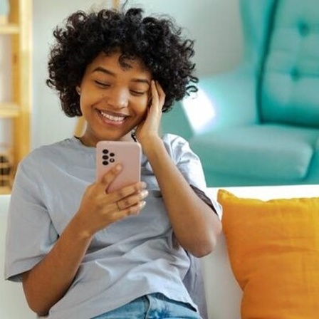 Eine junge Frau hält lächelnd ein Smartphone in der Hand