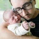 Vater mit Brille hat drückt seine Wange an schreiendes Baby, das er im Arm hält.