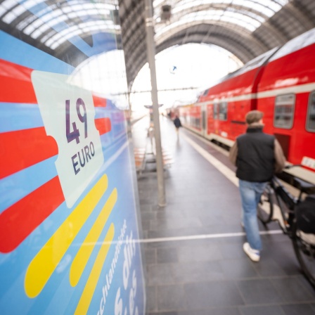 Ein Mann geht mit seinem Fahrrad an einer Deutschlandticket-Werbung und einem Regionalzug vorbei