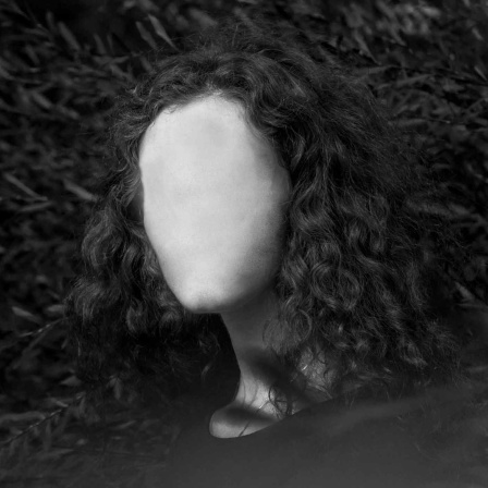 Schwarz-Weiß: Eine Frau mit langen schwarzen Haaren, ohne Gesicht.
