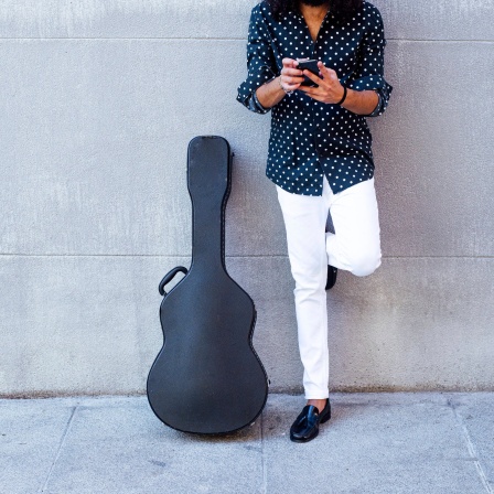 Guitarist using mobile phone while standing against concrete wall model released Symbolfoto