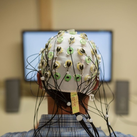 Ein Mann sitzt mit Elektroden auf dem Kopf vor einem Bildschirm.