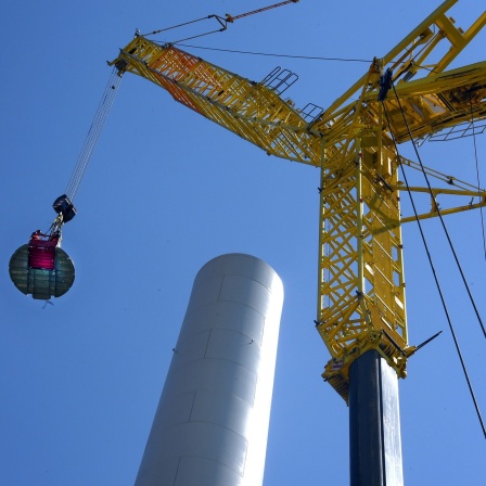 Ein Kran mit einer Plattform auf den Stahlbetonturm einer im Bau befindlichen Windkraftanlge gezogen.