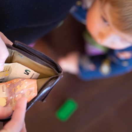 Eine Mutter schaut in eine Geldbörse, während ein Kind vor ihr steht.