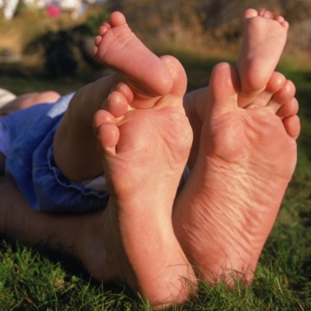 Ein Vater und Kind liegen im Gras und ruhen sich, die Füße weit von sich gestreckt, aus.