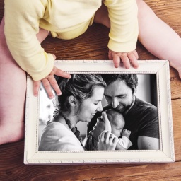 Ein Baby hält ein schwarz-weißes Familienfoto im Rahmen in den Händen