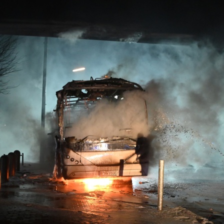 Feuerwehrmänner löschen an der Sonnenallee einen Reisebus, der von Unbekannten angezündet worden war. 
