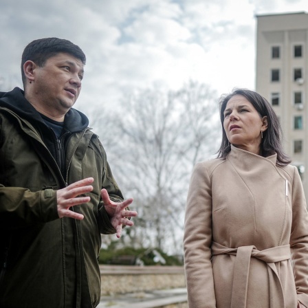 Außenministerin Annalena Baerbock (Grüne) und der Gouverneur der ukrainischen Oblast Mykolajiw, Witalij Kim, stehen vor dem zerstörten ehemaligen Sitz der Regionalverwaltung.