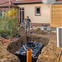Ein Mann verbaut im Garten neben seinem Haus eine Wasserzisterne, um seinen Garten mit Regenwasser bewaessern zu koennen.