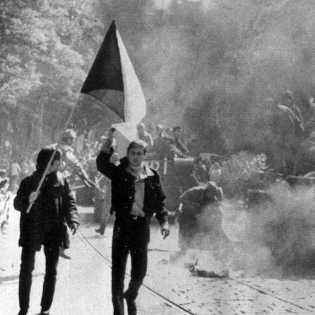 Demonstranten mit der tschechischen Flagge laufen am 21. August 1968 in Prag neben einem brennenden sowjetischen Panzer.