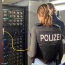 Polizistin steht vor einem Serverschrank mit gelber Kabelverbindung