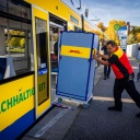 Ein Mitarbeiter der Deutschen Post schiebt einen Transportwagen für Pakete in eine Straßenbahn.