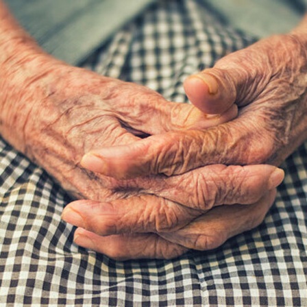 Eine alte Frau hat ihre Hand zusammengefaltet auf ihrem Schoß liegen.