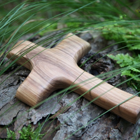 Holzkreuz unter Gräsern auf einem Baumstamm. 