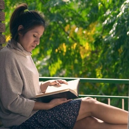 Eine Frau liest ein Buch im Rahmen ihres Fensters.