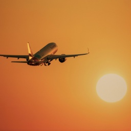 Flugzeug fliegt in Richtung einer großen, orange leuchtenden Sonne (Bild: picture alliance/imageBROKER/Lilly)