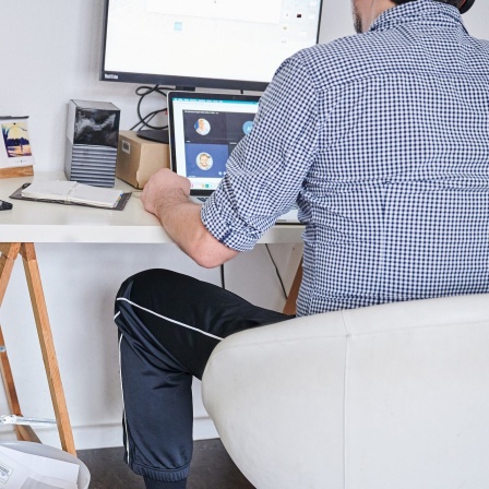 Ein Mann nimmt an einem Online-Meeting teil, während er oben herum ein Hemd trägt und unten herum eine Jogginghose. 