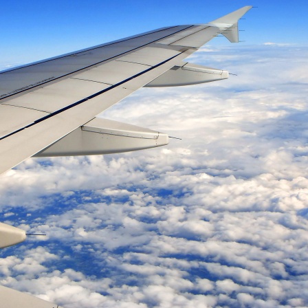 Flugzeuflügel vor blauem Himmel über der Erde und den Wolken, aus Flugzeugfenster gesehen.