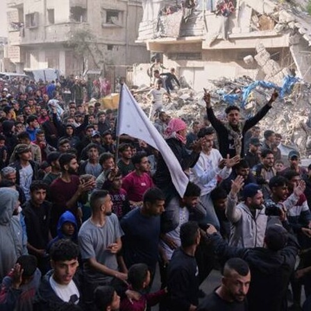 Palästinenser demonstrieren gegen Krieg und die regierende Hamas in Beit Lahiya im nördlichen Gazastreifen. Im Hintergrund ein zerstörtes Gebäude. (26.3.2025)