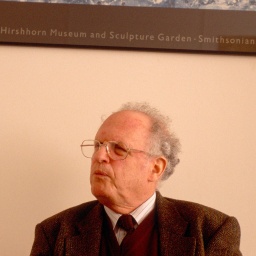Georges-Arthur Goldschmidt sitzt unter einem Plakat, Aufnahme aus dem Jahr 2002.