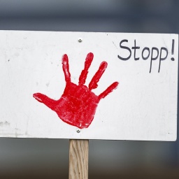 Auf einem weißen Schild ist ein roter Handabdruck sowie der Schriftzug "Stopp!".